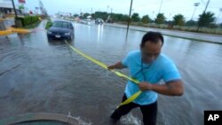 Mon Lun tira de una correa a su automóvil atascado por el agua antes de sacarlo de las aguas de inundación que retroceden en Dallas, el lunes 22 de agosto de 2022. (AP Photo/LM Otero)