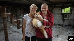 Zhanna Dynaeva and Serhiy Dynaev stand with a cat inside their house which was destroyed by Russian bombardment, in the village of Novoselivka, near Chernihiv, Ukraine, Aug. 13, 2022.