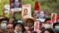 FILE - Demonstrators hold placards with pictures of Aung San Suu Kyi as they protest against the military coup in Yangon, Myanmar, Feb. 22, 2021. 