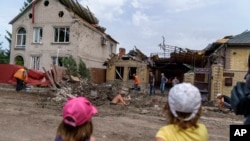 Children watch as workers clean up after a rocket strike on a house in Kramatorsk, Donetsk region, eastern Ukraine, Aug. 12, 2022.