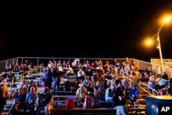 A crowd sits in a bleacher near the Saturn V visitor center several hours before the scheduled NASA moon rocket launch for the Artemis 1 mission to orbit the Moon at the Kennedy Space Center, Monday, Aug. 29, 2022, in Cape Canaveral, Fla. (AP Photo/Brynn