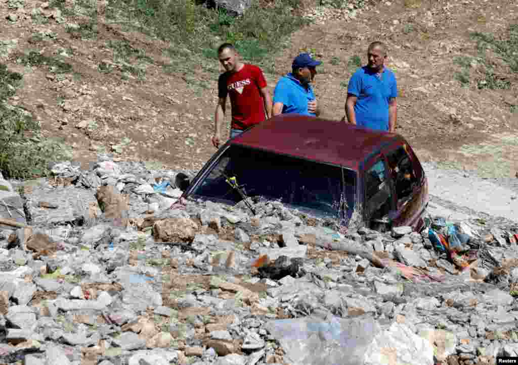 People work near a damaged car from the overnight floods in the village of Gjermo, North Macedoni.