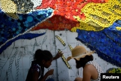 Para sukarelawan menggunakan tutup botol untuk mural ramah lingkungan berwarna-warni karya seniman Venezuela Oscar Olivares untuk meningkatkan kesadaran akan daur ulang, di Caracas, Venezuela, 19 Agustus 2022. (REUTERS/Gaby Oraa)