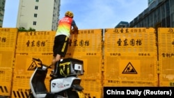 中國海南省三亞市一名快遞員站在電動機車上給防控區的人隔著圍板遞送快遞。 (2022年8月6日)