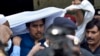 Police officers escort Shahbaz Gill, center in blue shirt, a political aide to former Pakistani prime minister Imran Khan, after a court appearance, in Islamabad, Aug. 22, 2022.
