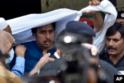 Police officers escort Shahbaz Gill, center in blue shirt, a political aide to former Pakistani prime minister Imran Khan, after a court appearance, in Islamabad, Pakistan, Aug. 22, 2022.
