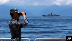 FILE - In this photo provided by China's Xinhua News Agency, a People's Liberation Army member looks through binoculars during military exercises as Taiwan's frigate Lan Yang is seen at the rear, Aug. 5, 2022. (Lin Jian/Xinhua via AP)