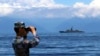 FILE - In this photo provided by China's Xinhua News Agency, a People's Liberation Army member looks through binoculars during military exercises as Taiwan's frigate Lan Yang is seen at the rear, Aug. 5, 2022. (Lin Jian/Xinhua via AP)