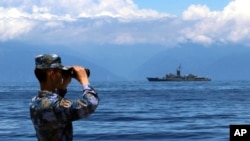 FILE - In this photo provided by China's Xinhua News Agency, a People's Liberation Army member looks through binoculars during military exercises as Taiwan's frigate Lan Yang is seen at the rear, Aug. 5, 2022. (Lin Jian/Xinhua via AP)