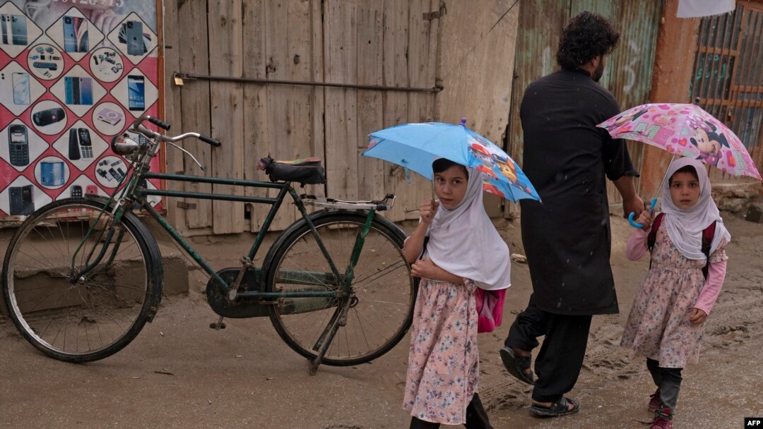 Dua orang anak perempuan Afghanistan berjalan menggunakan payung di jalanan Distrik Bagram, Provinsi Parwan, pada 25 Agustus 2022. (Foto: AFP/Wakil Kohsar)