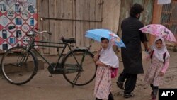 Dua orang anak perempuan Afghanistan berjalan menggunakan payung di jalanan Distrik Bagram, Provinsi Parwan, pada 25 Agustus 2022. (Foto: AFP/Wakil Kohsar)