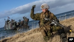 In this image provided by the North Atlantic Treaty Organization, a U.S. Marine waves his troops onward after using a Dutch landing craft to land near Sandstrand, Norway, March 21, 2022, during the Exercise Cold Response 22.