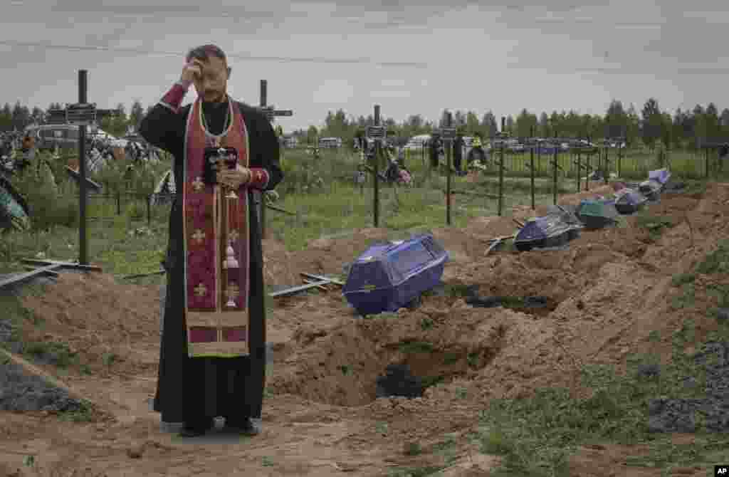 A priest prays for unidentified civilians killed by Russian troops, in Bucha, near Kyiv, Ukraine.