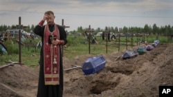 FILE: A priest prays for unidentified civilians killed by Russian troops during Russian occupation in Bucha, on the outskirts of Kyiv, Ukraine. Taken 8.11.2022