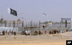 FILE - Pakistan and Taliban flags flutter on their respective sides while people walk through a security barrier to cross border at a key border crossing point between Pakistan and Afghanistan, in Chaman, Pakistan, Aug. 18, 2021.