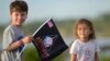 A child waves a souvenir flag while waiting on the Max Brewer Bridge to view the launch on Pad 39B for the Artemis I mission to orbit the moon at the Kennedy Space Center, Aug. 29, 2022, in Titusville, Florida.