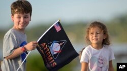 A child waves a souvenir flag while waiting on the Max Brewer Bridge to view the launch on Pad 39B for the Artemis I mission to orbit the moon at the Kennedy Space Center, Aug. 29, 2022, in Titusville, Florida.
