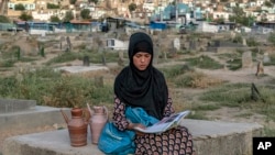 کابل کے ایک قبرستان میں پانی فروخت کر کے روزی کمانے والی چودہ سال کی سارا، فرصت کے وقت ایک کتاب پڑھ رہی ہے۔ اے پی فوٹو 