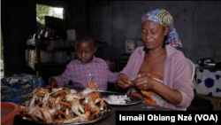 Charlotte Cocodji, avec son fils à ses côtés, nettoyant les crabes dans sa cuisine du Cap Estérias, au nord de Libreville, au Gabon. Août 2022.