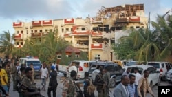 Vyombo vya usalama na watu wengine wakipita mbele ya Hotel Hayat iliyoharibiwa na shambulizi la kigaidi mjini Mogadishu, Somalia, Aug. 21, 2022. 