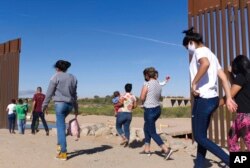 FILE - Brazilian migrants make their way around a gap in the U.S.-Mexico border in Yuma, Ariz., seeking asylum in the U.S. after crossing over from Mexico, June 8, 2021.