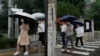 Office workers walk with umbrellas during a rainy day in Beijing, Aug. 18, 2022. Some were killed with others missing after a flash flood in western China Thursday, as China faces both summer rains and severe heat and drought in different parts of the country.