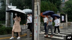 Office workers walk with umbrellas during a rainy day in Beijing, Aug. 18, 2022. Some were killed with others missing after a flash flood in western China Thursday, as China faces both summer rains and severe heat and drought in different parts of the country.