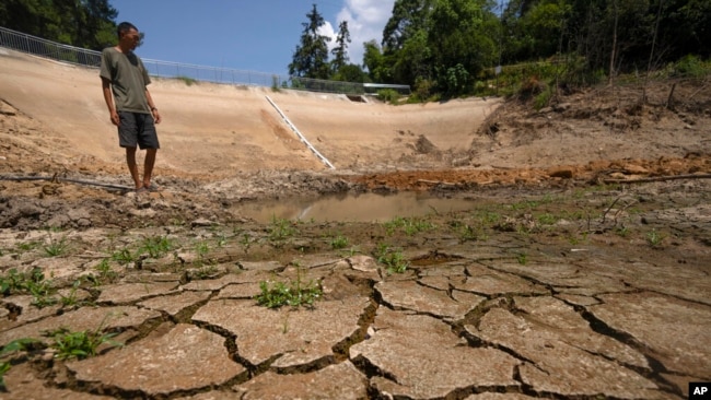 Gan Bingdong stands in a dried out community reservoir near his farm in Longquan village in southwestern China's Chongqing municipality on Aug. 20, 2022. (AP Photo/Mark Schiefelbein)