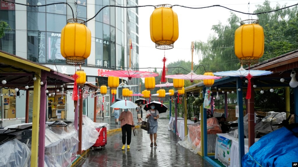 北京居民走过一家因大雨而暂停营业的露天市场。中国央行为提振经济调低了主要利率，为习近平争取第三期连任住一臂之力。(photo:VOA)