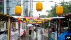 北京居民走過一家因大雨而暫停營業的露天市場。中國央行為提振經濟調低了主要利率，為習近平爭取第三期連任住一臂之力。