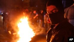 An anti-government protester stands next to burning tire during ongoing protests against the country's financial woes, in Beirut, Lebanon, Jan. 15, 2020.