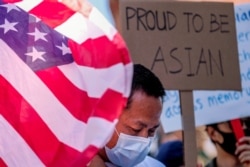 FILE - A demonstrator stands between a U.S. flag and a sign during a rally against anti-Asian hate crimes outside City Hall in Los Angeles, California, March 27, 2021.