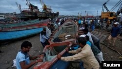 Fishermen move a fishing boat to a safer place along the shore ahead of the expected landfall of Cyclone Vayu at Veraval, India, June 12, 2019. 