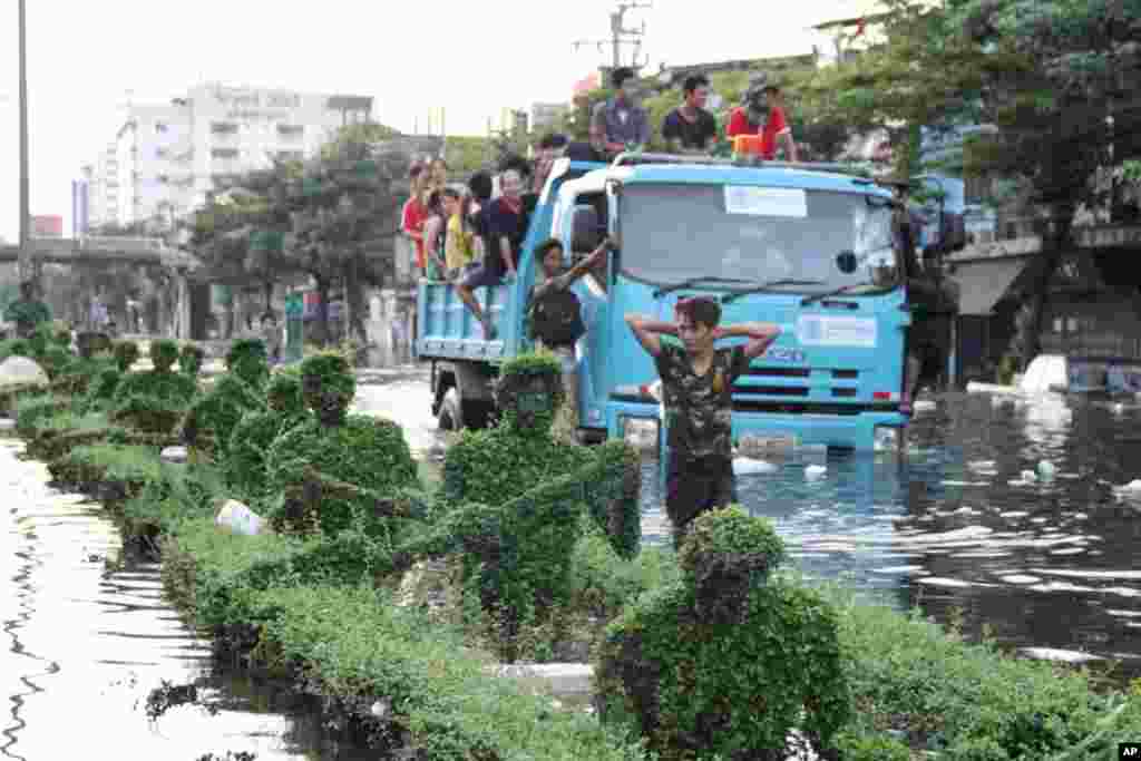 A resident evacuates flooded Bang Phlat, walking along the street near the boat and oarsman of the Royal Barge Museum's topiaries, Bangkok, October 31, 2011. (VOA)