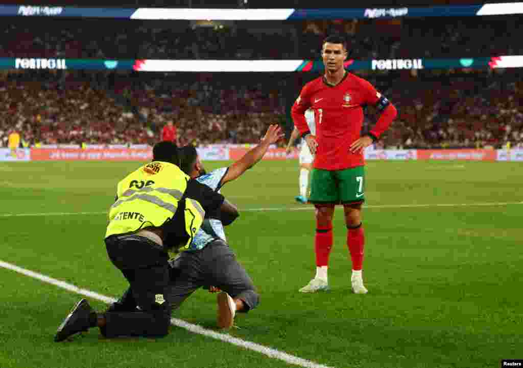 Pitch invader is detained as Portugal's Cristiano Ronaldo looks on during the League A football match between Portugal and Scotland in Lisbon, Portugal, Sept. 8, 2024.