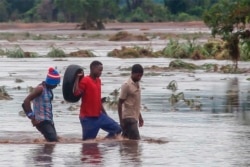 In this image made from video, people walk on a road swept by flooding waters in Chikwawa, Malawi, Jan. 25, 2022.