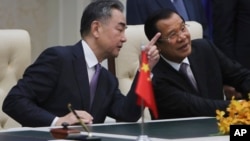 FILE - Chinese Foreign Minister Wang Yi, left, talks with Cambodian Prime Minister Hun Sen as they sit to witness a signing ceremony for a free trade agreement at Peace Palace in Phnom Penh, Cambodia, Monday, Oct. 12, 2020. (AP Photo/Heng Sinith)