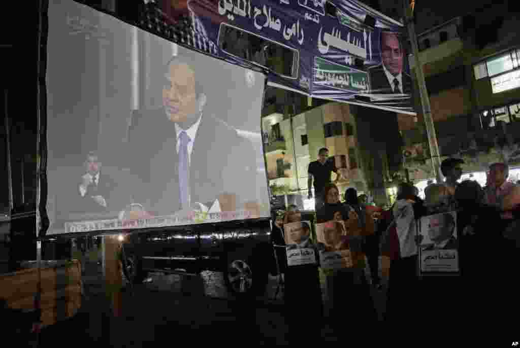 Para pendukung mantan komandan angkatan darat Abdel-Fattah el-Sissi menonton wawancara pertamanya yang disiarkan televisi dari sebuah layar di Kairo (5/5). (AP/Khalil Hamra)