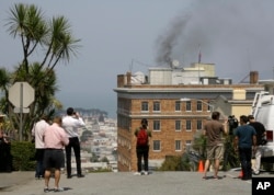 People stop to watch black smoke coming from the roof of the Consulate-General of Russia in San Francisco, Sept. 1, 2017.