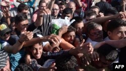 Migrants rise their hands to get some food and water distributed by Caritas on the Greek-FYR Macedonia border near the vilage of Idomeni, Sept. 5, 2015.