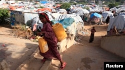 FILE - An internally displaced Somali girl carries a jerry-can of water as she walks through their makeshift shelters at Sayyidka camp in the Howlwadag district, south of Somalia's capital Mogadishu.