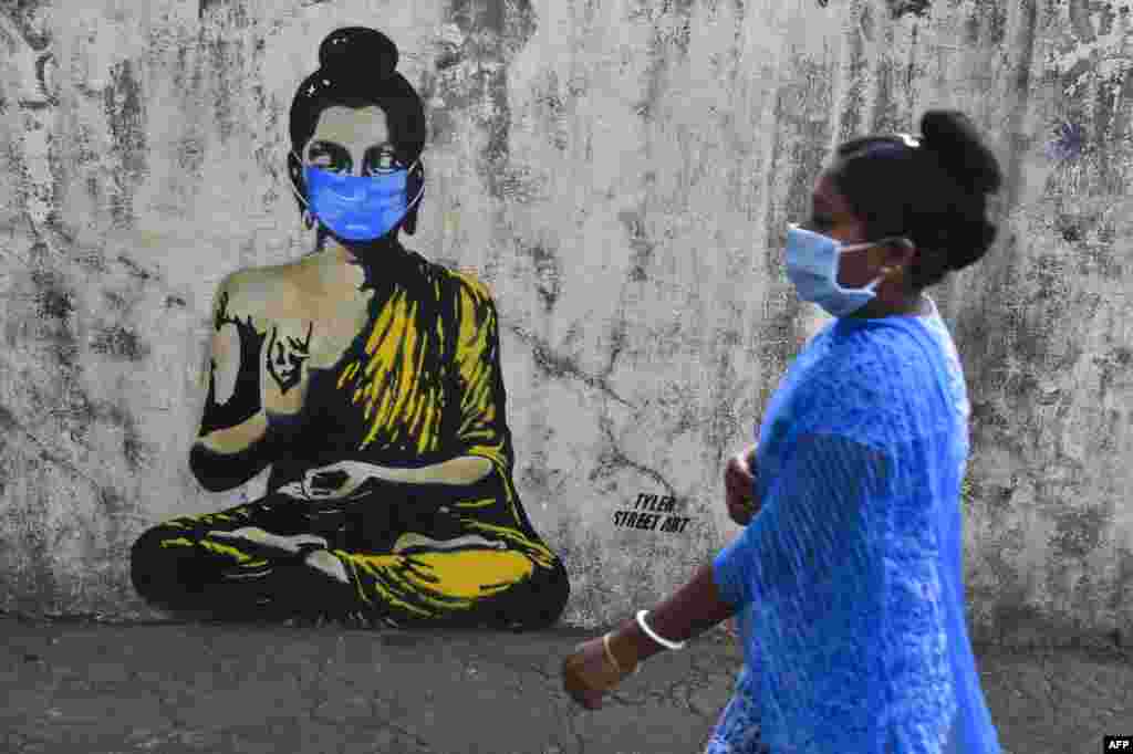 A resident wearing a facemask amid concerns over the spread of the coronavirus walks past a graffiti of Buddha wearing facemask, in Mumbai, India.
