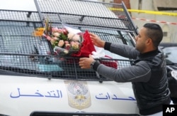 FILE - A man places a bouquet of flowers on a police van, near the bus that exploded Tuesday in Tunis, Nov. 25, 2015.