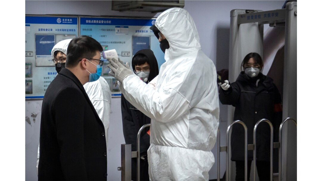 Seorang petugas medis mengenakan baju hazmat memeriksa suhu tubuh seorang penumpang di pintu masuk stasiun bawah tanah di Beijing, China, 26 Januari 2020.
