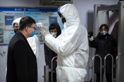 Seorang petugas medis mengenakan baju hazmat memeriksa suhu tubuh seorang penumpang di pintu masuk stasiun bawah tanah di Beijing, China, 26 Januari 2020.