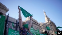 An abortion-rights activist in favor of an abortion bill holds a green bandana symbol the the abortion-rights movement, in a demonstration outside the legislative building in Buenos Aires, Argentina, Dec. 17, 2020.