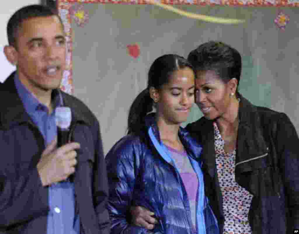 First lady Michelle Obama (R) stands with her daughter Malia (2nd R) as U.S. President Barack Obama (L) delivers remarks during a day of service to honor Martin Luther King, Jr, at the Browne Education Campus school in Washington, January 16, 2012. REUTER