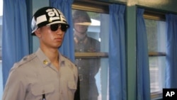 Một binh sĩ Bắc Triều Tiên nhìn qua khung cửa sổ, trong lúc một binh sĩ Nam Triều Tiên đứng gác tại làng Bàn Môn Điếm, 21/7/2010
