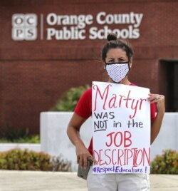 FILE - In this Tuesday, July 7, 2020 file photo, Rachel Bardes holds a sign in front of the Orange County Public Schools headquarters as teachers protest with a car parade in Orlando, Fla. (Joe Burbank/Orlando Sentinel via AP, File)