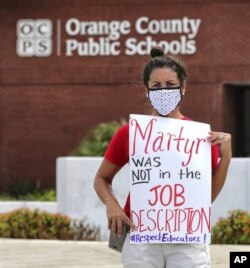 FILE - In this Tuesday, July 7, 2020 file photo, Rachel Bardes holds a sign in front of the Orange County Public Schools headquarters as teachers protest with a car parade in Orlando, Fla. (Joe Burbank/Orlando Sentinel via AP, File)